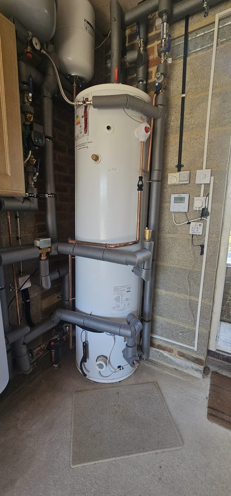 Close view of a hot water cylinder with copper connections and insulated pipe runs